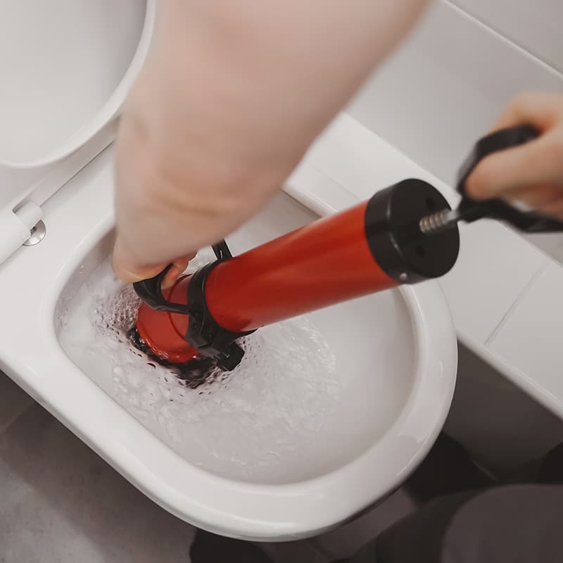 a Chipper Plumbing expert clearing a toilet line with a force pump