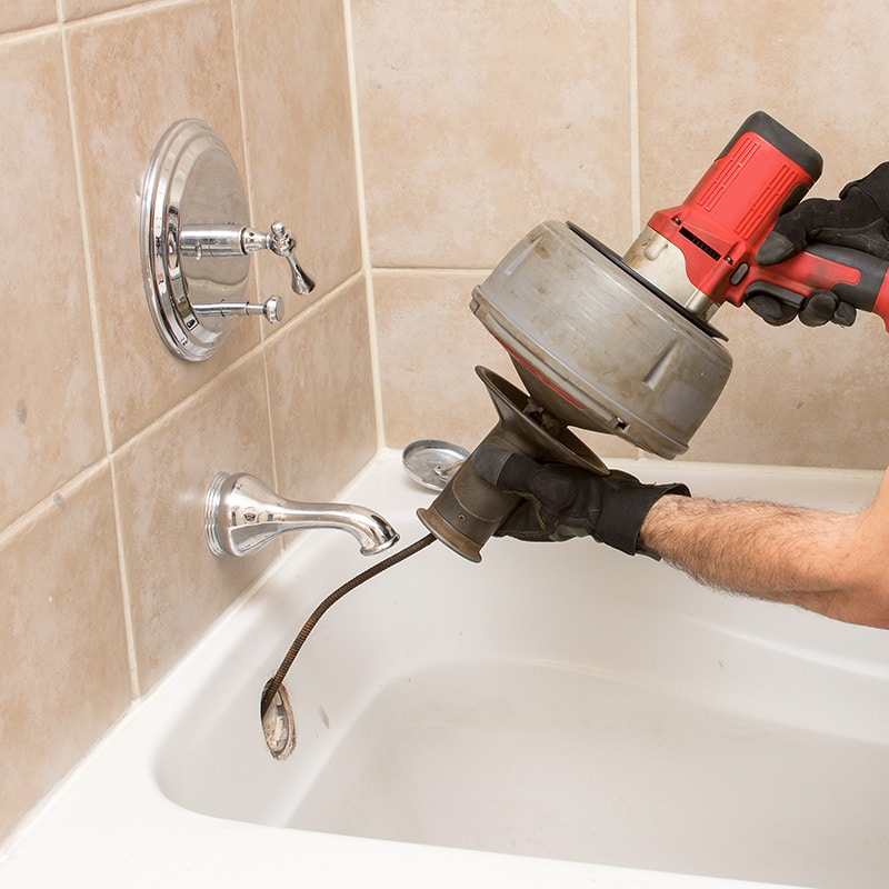 a Chipper Plumbing & Radiant expert clearing a bathtub drain with a snake tool